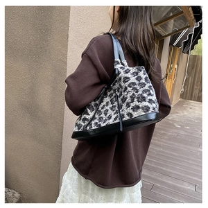 Detail of plush leopard print tote bag with black leather handle in an outdoor lifestyle setting