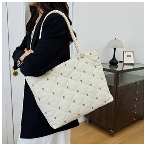 Detail of quilted canvas tote bag featuring small brown bows and thick rope shoulder strap