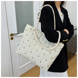 Detail of white quilted tote bag with brown bow embroidery and braided rope handles