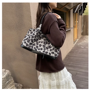Detail of leopard print plush tote bag with black leather straps on woman's shoulder