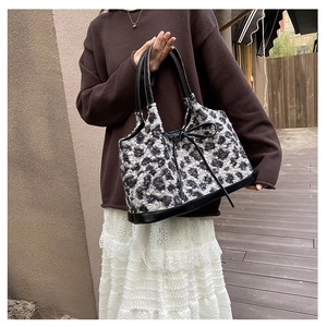 Outdoor shot of a plush leopard print tote bag with black leather straps and bow detail