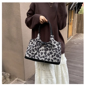 Detailed close-up of leopard print plush tote bag featuring black leather handles and bow