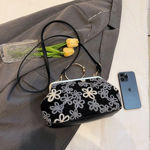 Sac à main vintage brodé de fleurs avec poignée dorée posé sur un blazer élégant