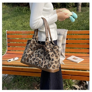 Detailed view of the plush leopard print tote bag with brown leather base on park bench