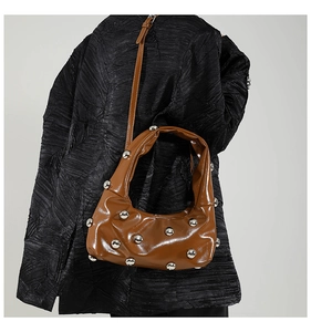 Detail of brown glossy crescent bag with silver rivets and adjustable shoulder strap