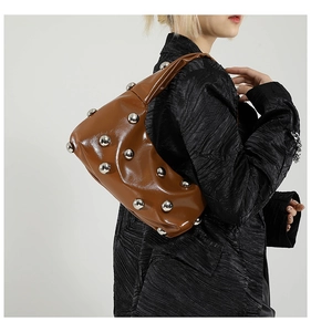 Close-up of brown leather shoulder bag with decorative silver rivets on a model