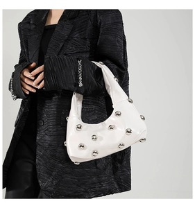Detail of silver rivets on white leather crescent bag shown against dark blazer