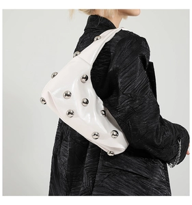 Detail of white dumpling bag with silver metal ball studs on a black textured jacket