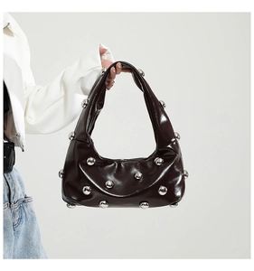 Detail shot of a dark brown glossy dumpling bag featuring metallic silver ball rivets