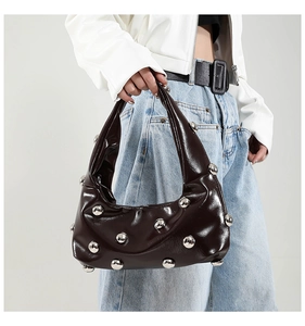 Detail of dark brown patent leather dumpling bag featuring large silver spherical metal rivets
