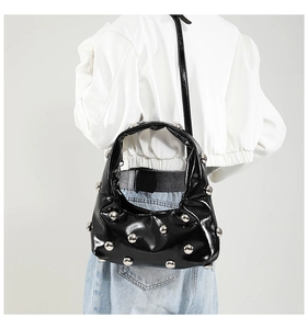 Detail of black patent leather shoulder bag with silver studs and rivet texture