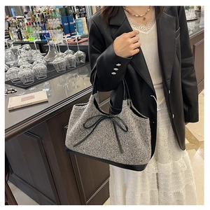 Close-up of grey tweed tote bag featuring a leather bow accent and black handles
