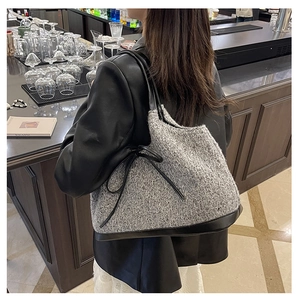Detail view of grey knit shoulder bag with black leather trim and bow drawstring accents