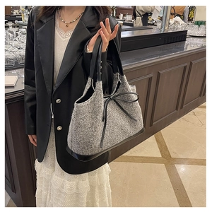 Detail of grey tweed tote bag featuring black leather bow and handle on model arm