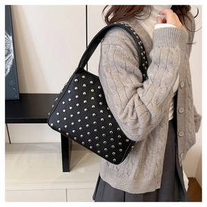 Detail of silver rivets on a black PU leather shoulder bag worn by a model