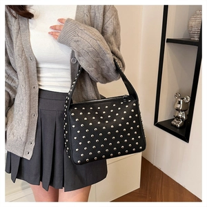 Close-up of black pebble leather handbag with silver rivets worn over the shoulder