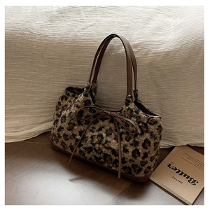 Detailed view of plush leopard print handbag with leather straps and a decorative bow