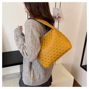 Detail view of bright yellow leather shoulder bag with silver punk rivets on model