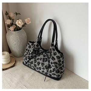 Detail of leopard print plush handbag with black leather handle and a delicate bow accent