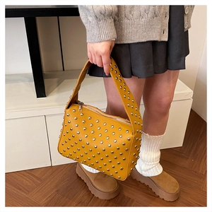 Detail of yellow pebbled leather handbag featuring silver sphere studs and wide top handle