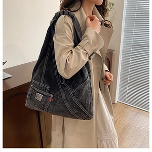 Détail du sac fourre-tout en denim délavé avec surpiqûres contrastées et poche zippée avant