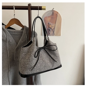 Detail of grey knit handbag featuring a black leather bow and textured tweed finish
