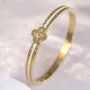 Detailed macro view of a gold-plated clover bangle with white enamel inlay accents