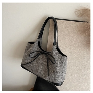 Detailed view of grey tweed tote bag featuring black leather handles and a delicate bow detail