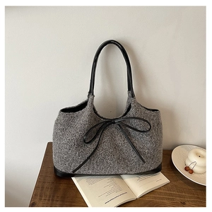 Detail of grey knitted tote bag featuring a black leather bow and elegant woven texture