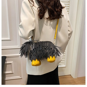 Detail shot of a black fringed puppy-shaped crossbody bag with yellow accents on a white blazer