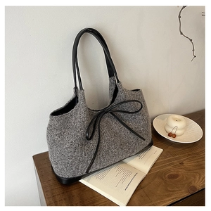 Detail of grey knitted tote bag featuring black leather straps and a delicate bow accent