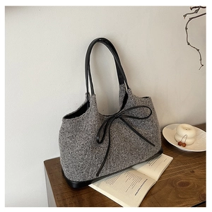 Macro detail of grey knitted tote bag featuring black leather trim and bow decoration