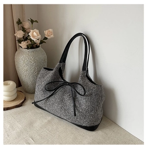 Close-up of grey plush tote bag with black leather bow detail and sturdy bottom base
