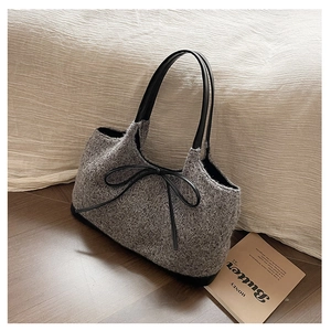 Detail of grey bouclé tote bag with black bow decoration on warm wood background