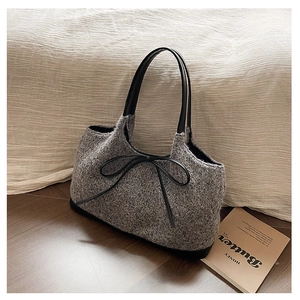 Detail of grey tweed tote bag featuring black leather bow and elegant handle design