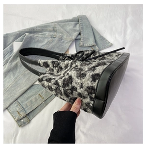 Close-up of leopard print plush tote bag with black leather straps and denim jacket