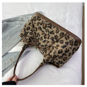 Detail view of leopard print plush handbag with brown leather strap on white fabric