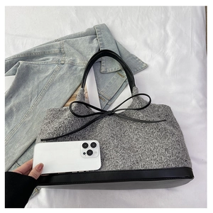 Detail of grey knit tote bag with black leather trim and bow on white cloth