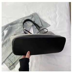 Detail of the gray plush tote bag featuring a durable black leather base and stitching