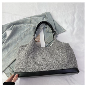 Detail of grey tweed tote bag with black leather base and handles on denim jacket