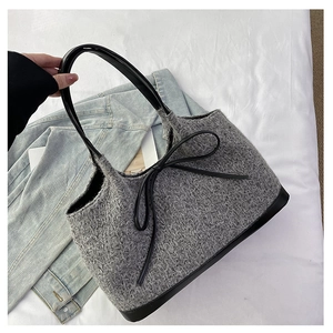 Detail of grey knitted tote bag featuring a decorative black leather bow and handle
