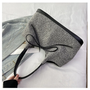 Detail of grey plush tote bag with black leather trim and bow on white fabric