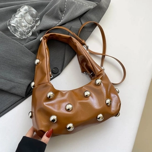 Caramel hobo bag with large silver studs and slouchy leather texture on grey suit