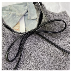 Detail of grey plush handbag featuring a black bow and textured fabric on denim background