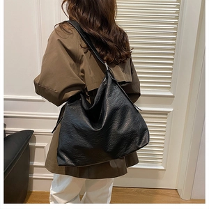 Model wearing a large black soft leather tote bag with natural wrinkled texture and wide strap