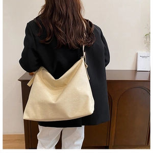 Detail of the soft beige leather texture and wide strap of the large tote bag on a model