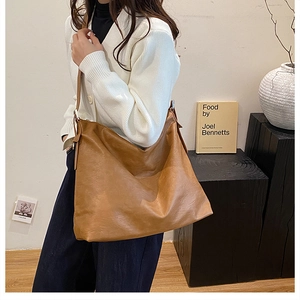 Brown leather large capacity tote bag shown on model in a minimalist indoor setting