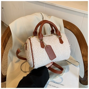 Detail view of cream plush Boston bag with brown leather handles on a wooden chair