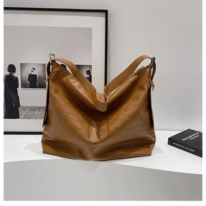 Close-up of brown textured leather tote bag featuring a wide strap and metal buckle