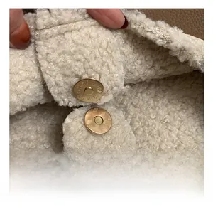 Macro shot of golden magnetic buckle on cream faux shearling with brown leather trim
